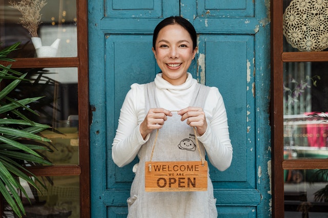 imagem de microempreendedora em frente ao seu negócio segurando placa de aberto