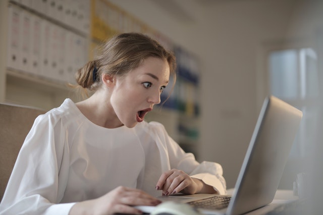 Mulher em camisa branca de manga comprida usando computador laptop prateado
