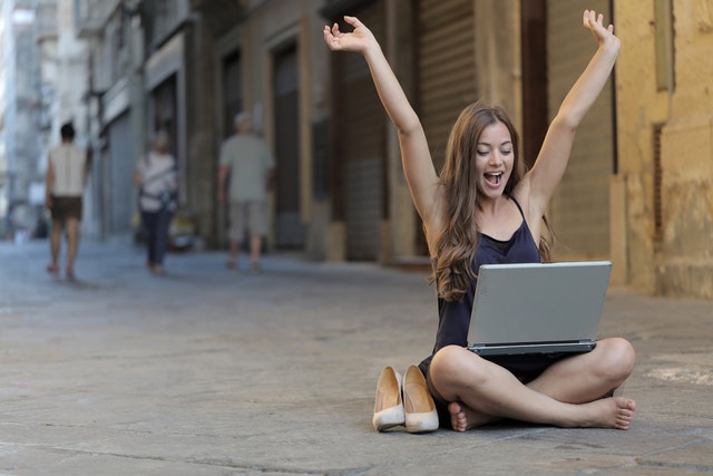 Mulher levantando as mãos enquanto está sentada no chão com um macbook pro no colo