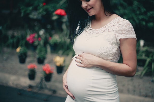 Imagem de mulher grávida em vestido branco segurando o estômago
