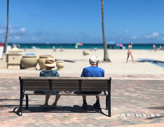 Imagem de um casal de idosos sentados em um banco na praia olhando o mar