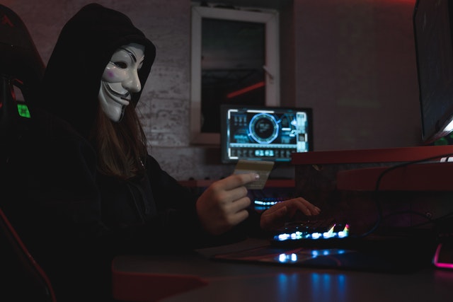 imagem de hacker com mascara do V de vingança com um cartão de crédito na mão