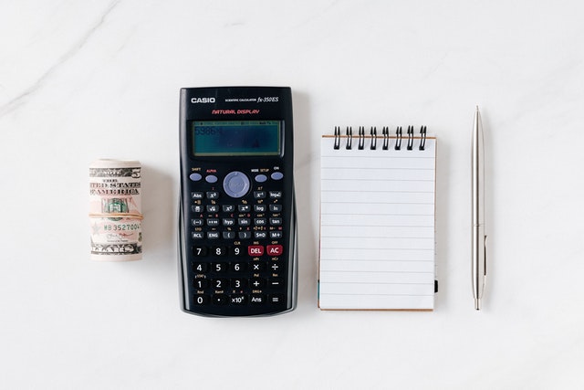 Imagem de calculadora ao lado de um bloco de anotações e um rolo de dinheiro