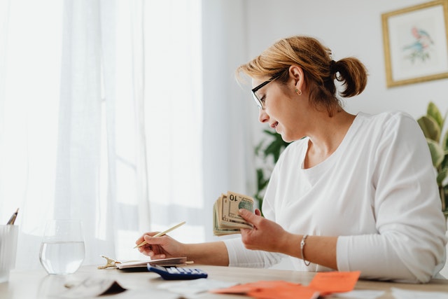 Imagem de mulher fazendo cálculos e com dinheiro em sua mão